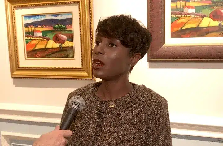 Woman speaking into a microphone in an art gallery with framed landscape paintings behind her