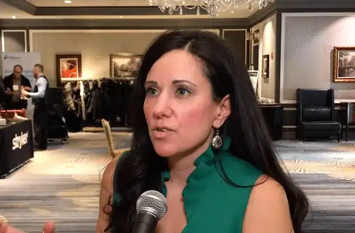 Woman in a green sleeveless top being interviewed with a microphone at a conference venue